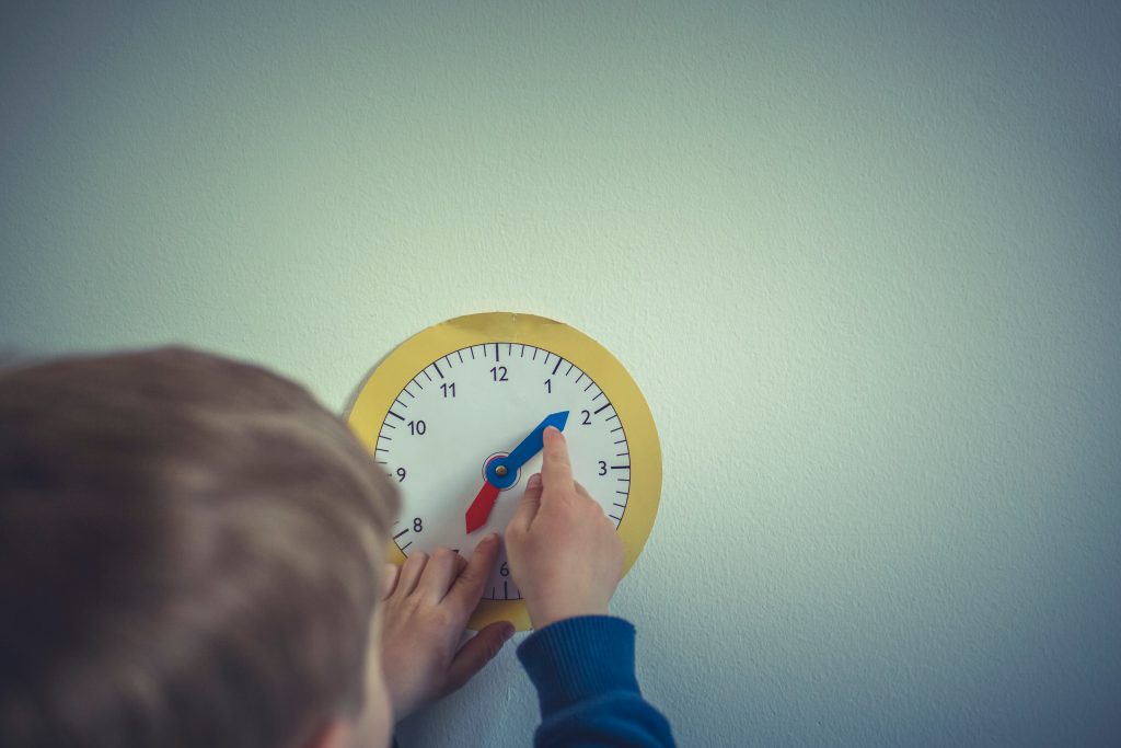 enfant qui tourne les aiguilles d'une horloge pour apprendre à lire l'heure