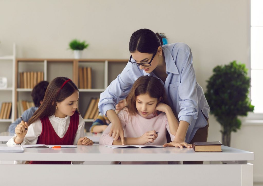 enseignante en classe en train d'aider des élèves dans leurs travaux d'écriture