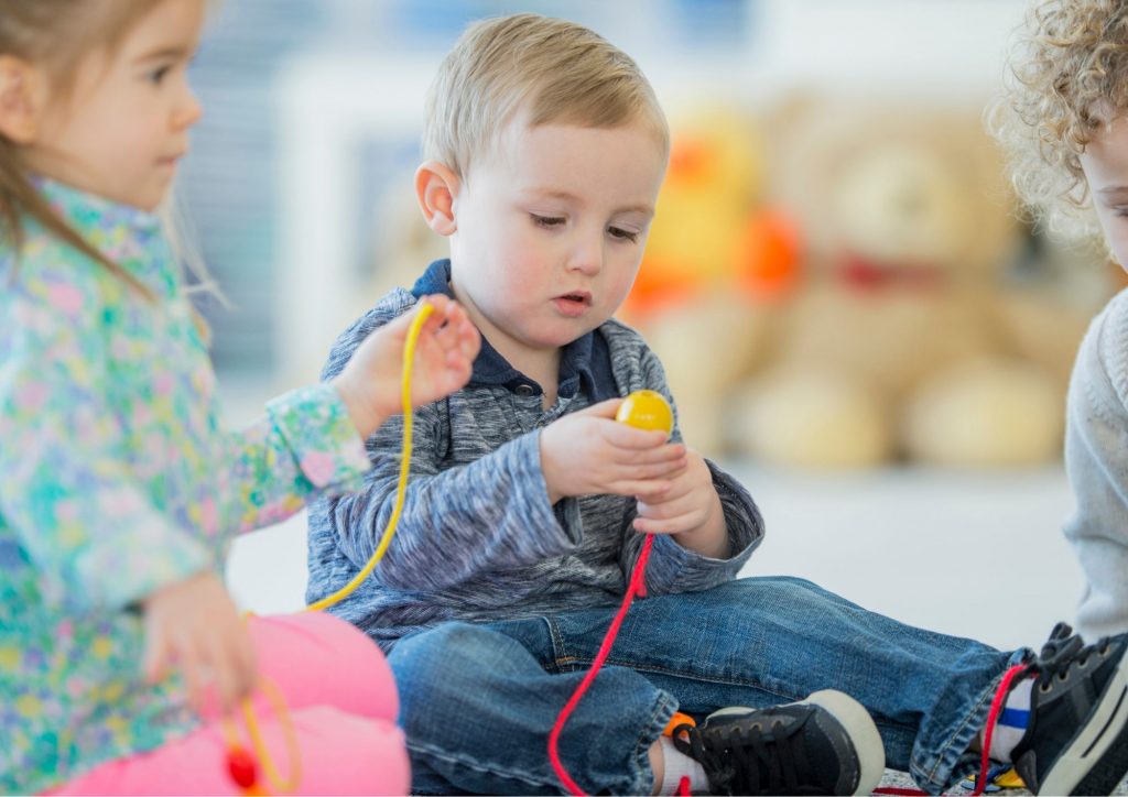 enfants quu enfilent des perles motricité fine