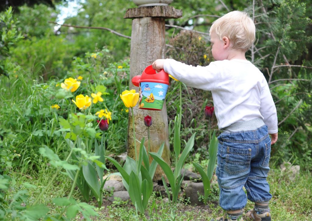 jeune enfant qui arrose le jardin
